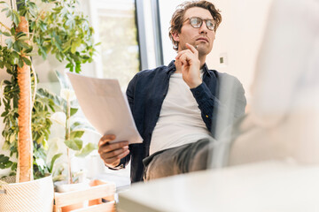 Thoughtful mid adult man writing on paper while sitting at home