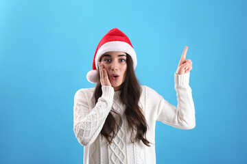 Fototapeta na wymiar Beautiful emotional woman wearing Santa Claus hat on light blue background
