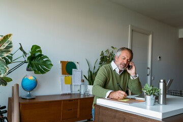 Mature man talking on mobile phone while working at home