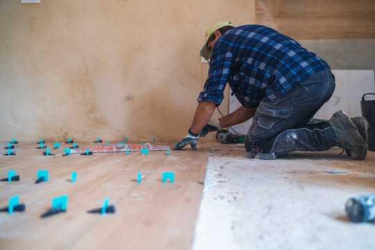 Male manual worker concentrating while working on parquet floor in house