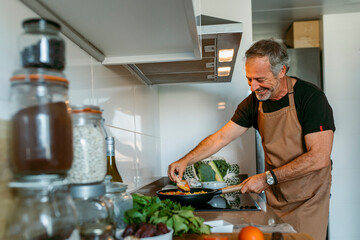 Happy mature man preparing pasta while standing in kitchen at home