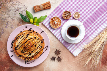 Fototapeta na wymiar Above view of delicious pancakes with chocolate syrop and a cup of tea on pink stripped towel
