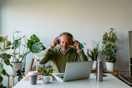 Smiling Man Wearing Headphones While Working On Laptop At Home