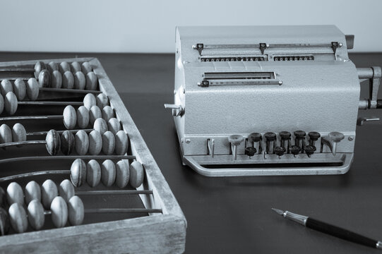 Old wooden abacus, mechanical calculator and fountain pen on a vintage desk.