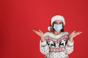 Fototapeta na wymiar Emotional woman in Santa hat and medical mask on red background, space for text