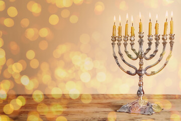Silver menorah with burning candles on wooden table against beige background, space for text. Hanukkah celebration