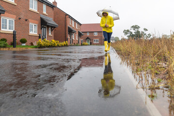 Woman holding umbrella walking in puddle on street during rainy season