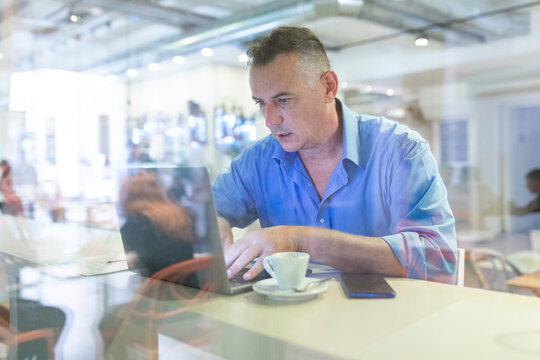 Male entrepreneur using laptop while sitting with coffee in cafe