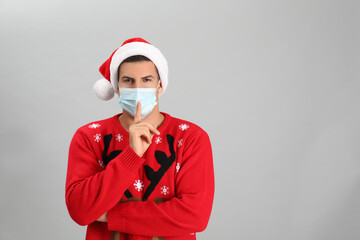 Man wearing Santa hat and medical mask on grey background, space for text