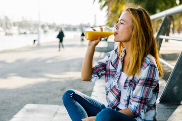 Young woman drinking juice while sitting on footpath in city