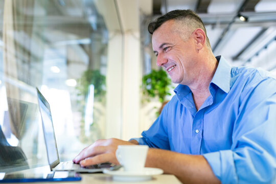 Smiling businessman using laptop while sitting at cafe
