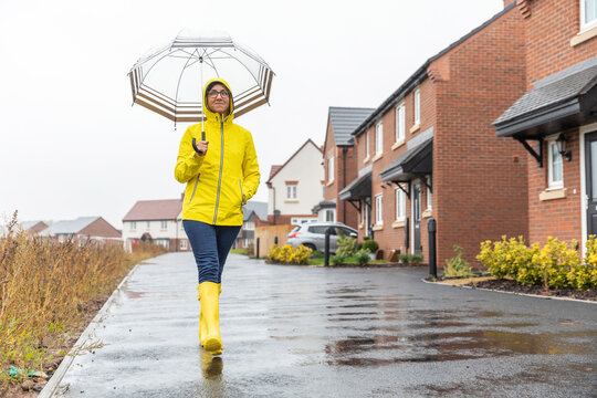 Woman with hands in pockets holding umbrella waking on street in city during rainy season
