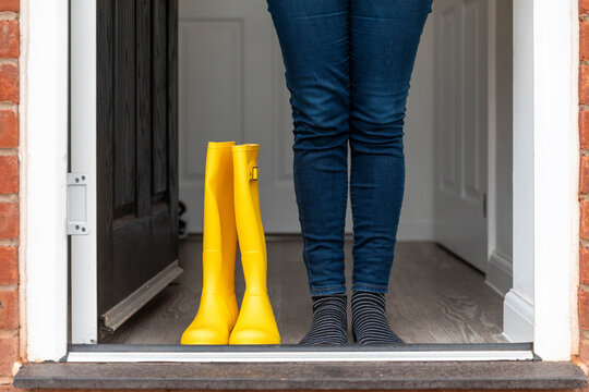 Legs of woman standing with rubber boot at home during rainy season