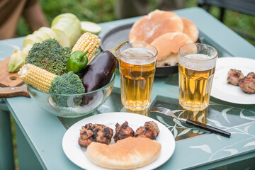 Close-up of a picnic table in the garden for two people. Food, grilled meat, grilled vegetables, beer