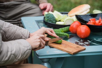 A couple in self-isolation have a barbecue and relax by watching interesting video blogs on their smartphone. In front of them is a table with snacks and beer