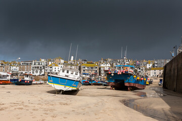 Fishing boats beached at low tide in St. Ives' Harbour, Cornwall, UK: rainstorm approaching.