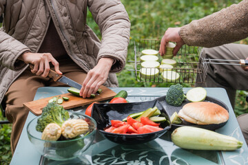 Still life shot, hands cutting vegetables on a cutting Board. Preparing for a family dinner on the lawn in front of a country house. Summer activities