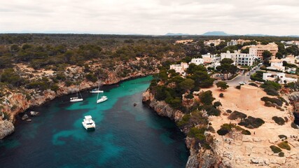 Fototapeta na wymiar Floating boats in crystal clear Mediterranean sea with coral reef and cliffs, Mallorca, Cala pi, Cala Satanyi, Aerial. High quality photo