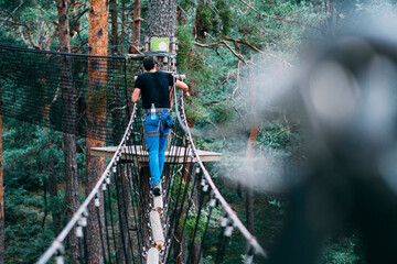 Young man crossing rope bridge in adventure park