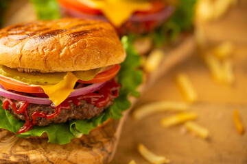 Top view of appetizing burgers with beef, tomato, lettuce, red onion, cheese, mustard and ketchup on wooden chopped board with french fries.