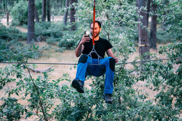 Excited young man photographing with mobile phone while enjoying zip line ride at adventure park