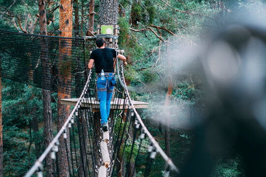 Fototapeta Young man crossing rope bridge in adventure park