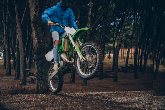 Teenage boy performing wheelie on dirt road in forest