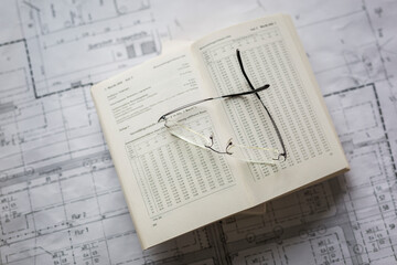 Book and eyeglasses over blueprint at desk