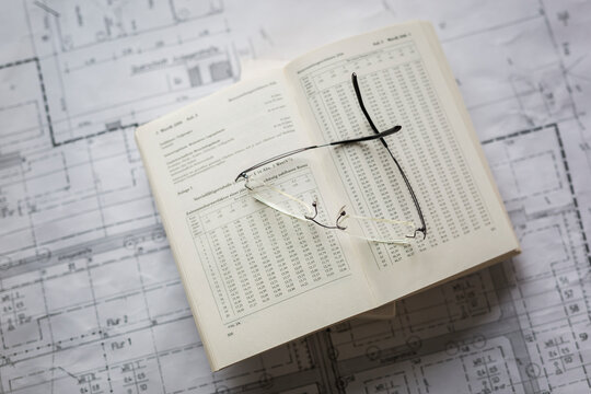 Book and eyeglasses over blueprint at desk