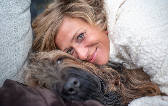 Smiling woman embracing Briard on sofa