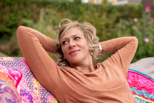 Smiling woman sitting with hands behind head on sofa at back yard