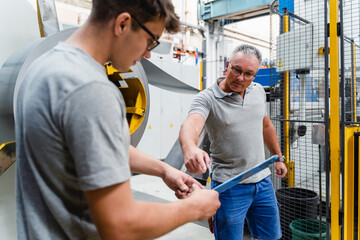Male coworkers brainstorming while standing against machinery in industry