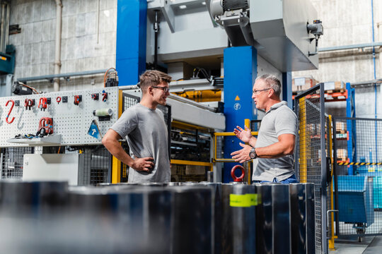 Mature male technician explaining colleague about machine at illuminated factory