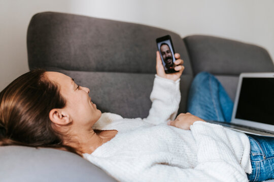 Smiling Woman Talking To Male Friend On Video Call Through Smart Phone At Home