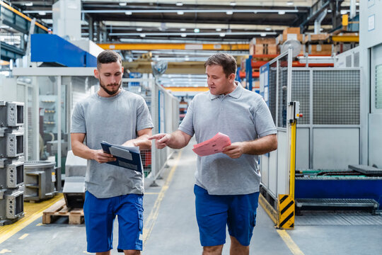 Mature manual worker discussing with young coworker at illuminated industry