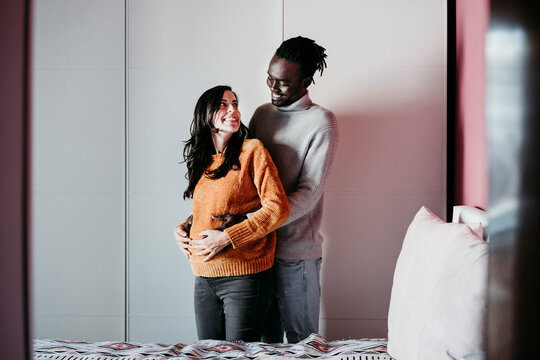Happy man embracing pregnant woman in bedroom at home