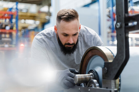 Mid adult male technician concentrating while analyzing machine part at factory