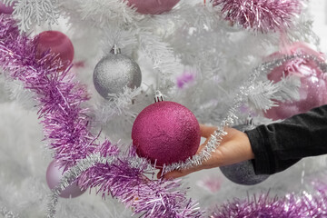 White Christmas tree. Child's hand touches balls on the Christmas tree. Close-up.