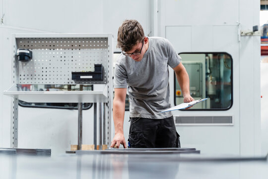 Male engineer holding clipboard while examining machinery in industry