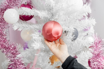 White Christmas tree. Child's hand touches balls on the Christmas tree. Close-up.
