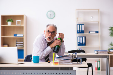 Old male employee drinking alcohol in the office