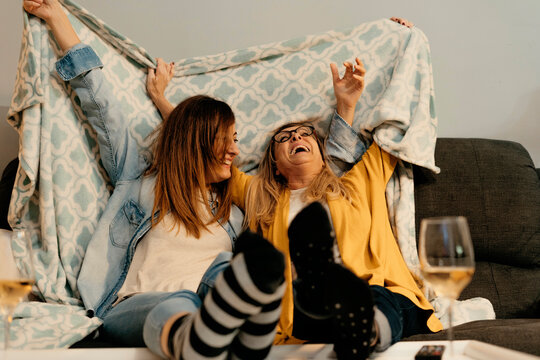 Happy daughter and mother holding blanket while sitting on sofa in living room