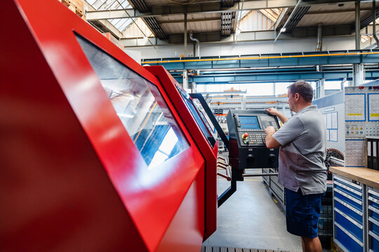 Professional male engineer operating control panel standing by machinery at industry