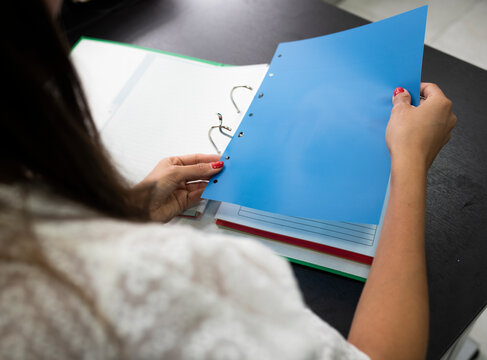 Businesswoman attaching paper in file while sitting on desk at office