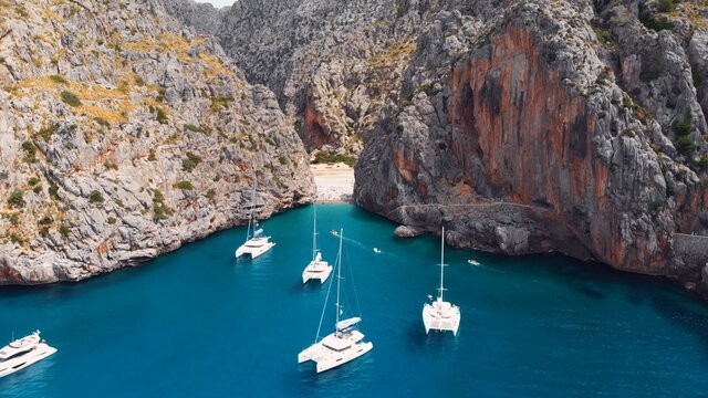 Serra De Tramuntana,Sa Calobra, Torrent De Pareis beach, aerial ,crystal clear water of mediterranean sea with moored sailing boats and yacht going towards the beach. High quality photo
