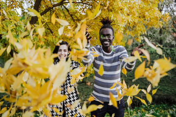 Happy multi ethnic couple throwing leaves while standing in park during autumn