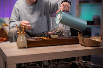 A young man fills a teapot with tea leaves with boiling water. The process of brewing strong asian tea according to eastern traditions