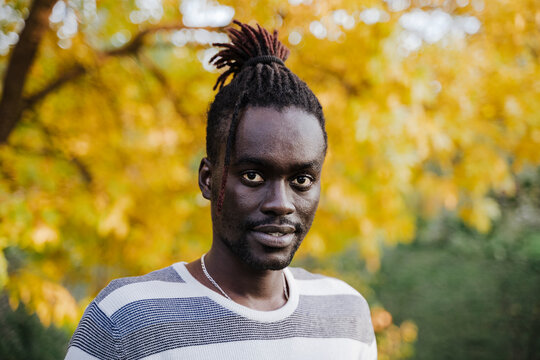 African man standing against yellow tree in park during autumn