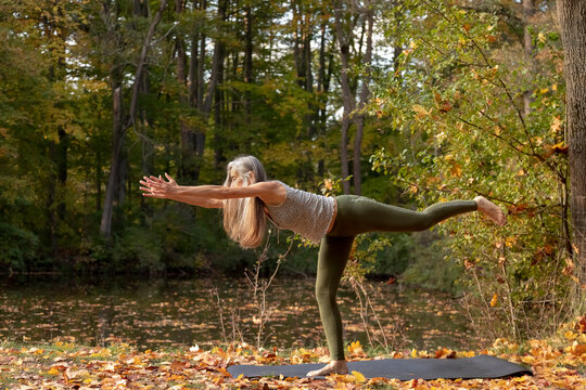 Mature woman practicing yoga by pond in park during autumn