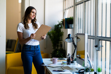 Smiling businesswoman holding clipboard while looking away in office